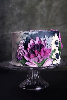 a multi - colored cake with flowers on it is sitting on a glass stand against a dark background