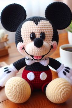 a crocheted mickey mouse sitting on top of a table next to a cup