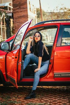 a woman sitting in the driver's seat of a red car talking on her cell phone