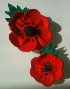 two red flowers with green leaves on white table top next to each other and one flower has black center