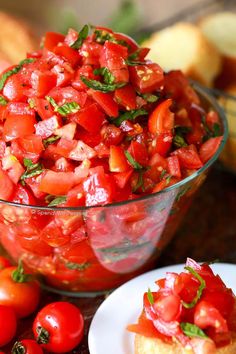 tomato salad in a glass bowl on a table with bread and cherry tomatoes around it