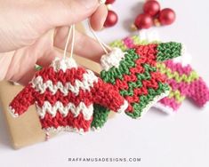 a hand is holding some crocheted ornaments on a piece of paper and string