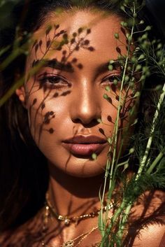 a woman with leaves on her face and chest is surrounded by greenery as she poses for the camera