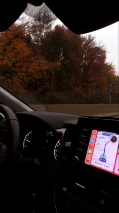 the dashboard of a car with an electronic device on it's display screen and trees in the background