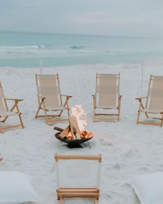 a fire pit on the beach with chairs around it