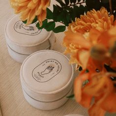 three round white boxes sitting on top of a table next to orange and yellow flowers