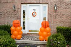 two orange balloons sitting in front of a white door with wreaths on the side