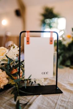 a close up of a sign on a table with flowers in front of it and an empty sheet of paper attached to the stand