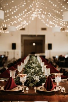 a long table is set with place settings and red napkins for the centerpiece