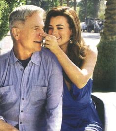 an older man and young woman sitting on a park bench, smiling at each other