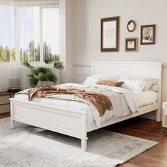 a white bed sitting in a bedroom on top of a hard wood floor next to a window