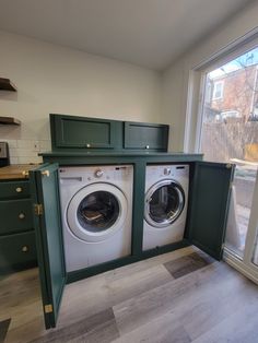 a washer and dryer in a kitchen next to an open window with green cabinets