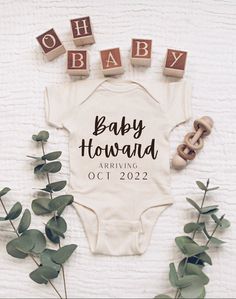 a baby bodysuit is surrounded by greenery and wooden blocks that spell out the word baby howard