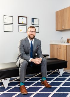 a man in a suit and tie sitting on a bench with his legs crossed, smiling at the camera