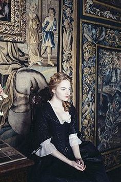 a woman is sitting on a chair in front of a wall with paintings and flowers