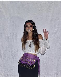 a woman with long hair wearing a purple skirt and white top is making the peace sign