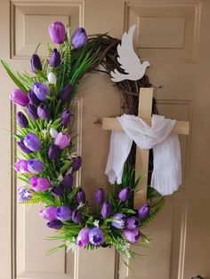 a wreath with purple and white flowers hanging on the front door next to a cross