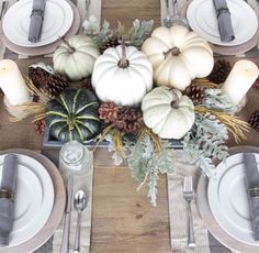 the table is set with white pumpkins, pine cones and greenery on it