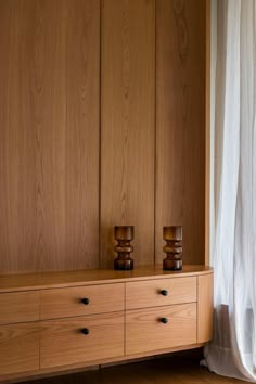 two candles sit on top of a wooden cabinet in front of a white drapes