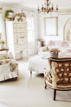 a bedroom with white walls and flooring has an ornate bed, chairs, and chandelier