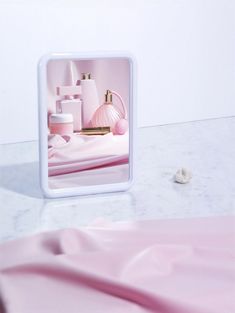 a mirror that is on top of a table next to a pink sheet and bottle