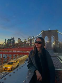 a woman standing on the side of a bridge next to a yellow taxi and cars