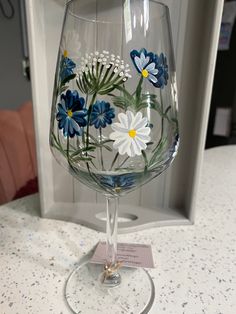 a wine glass with blue and white flowers painted on the side sitting on a counter