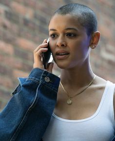 a woman talking on her cell phone while wearing a white tank top and denim jacket