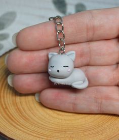 a small white cat keychain sitting on top of a piece of wood in someone's hand