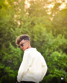 a young man wearing sunglasses standing in front of trees