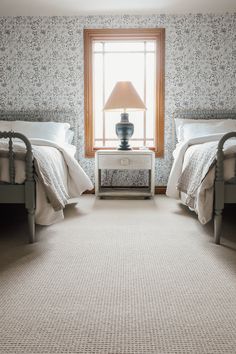 two beds in a room with floral wallpaper and a lamp on the end table