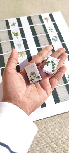 a person's hand holding two small pieces of paper with plants printed on them