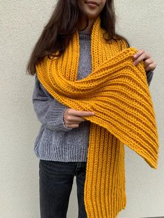 a woman wearing a yellow knitted shawl with her hands on her hips, standing in front of a white wall