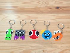 four pixel keychains are shown on a wooden surface, each with different characters