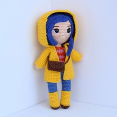 a crocheted doll wearing a yellow raincoat and red striped scarf, standing against a white wall