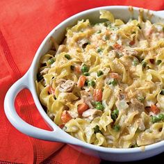 a casserole dish with chicken, peas and carrots in it on a red cloth