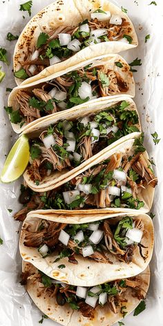 four tacos with shredded meat, cilantro and onions on a white tray