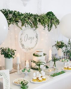 a table topped with lots of white balloons and plates filled with food next to greenery