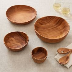 wooden bowls and utensils are laid out on a white tablecloth with wine glasses in the background