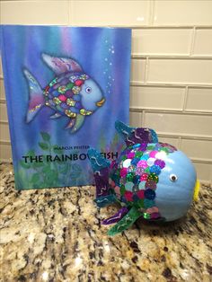 the rainbow fish is next to a book and some decorations on a counter top in front of a tile wall