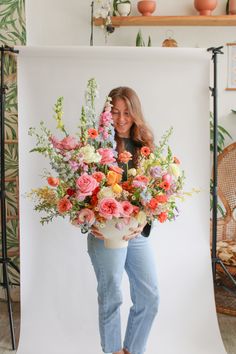 a woman holding a bouquet of flowers in front of a white backdrop for a photo shoot