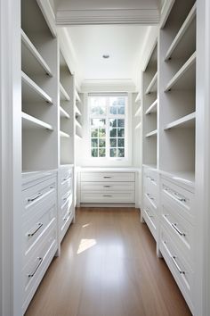 an empty walk in closet with lots of white drawers and shelving unit doors open