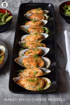 baked mayo - cheese mussels on a black platter next to bowls of salad