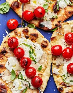 three pizzas with cherry tomatoes and mozzarella cheese on blue platter ready to be eaten