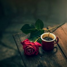 a red rose sitting next to a cup of coffee on top of a wooden table