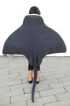 a woman is hiding her head under a large shark shaped pillow on the sidewalk while wearing high heels