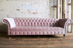 a pink velvet chesterfield style sofa against a white brick wall in an old warehouse building