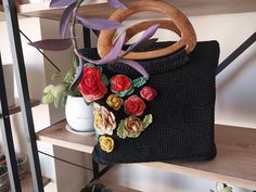 This hand-knitted black crochet bag is a true statement piece. Featuring vibrant, intricately crocheted floral designs on the front, it adds a beautiful contrast and pop of color to the elegant black base. The sturdy wooden handles provide a rustic, natural touch while ensuring durability and comfort for everyday use. Spacious and stylish, this unique accessory blends a chic, handmade aesthetic with practicality, making it perfect for casual outings or special occasions. Elevate your wardrobe wi Black Handmade Bohemian Crochet Bag, Handmade Black Crochet Bag As A Gift, Handmade Black Crochet Bag As Gift, Black Handmade Crochet Bag For Gift, Handmade Black Crochet Bag For Gift, Black Crochet Bags As Gift, Black Crochet Bag As Gift, Black Hand-knitted Crochet Bag For Daily Use, Black Crochet Bag