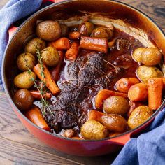 pot roast with carrots, potatoes and gravy in a red pan on a wooden table