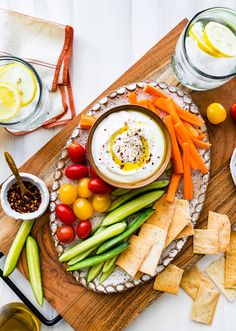 an assortment of vegetables and dips on a platter with crackers, lemon wedges, tomatoes, celery, cucumbers